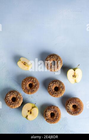 Hausgemachte gebackene Apfelmost-Donuts mit Zucker und Apfel auf blauer Strukturoberfläche schneiden. Bereit, Snack zu essen. Kleine Charge Lebensmittel mit Zutat. Direkt darüber Stockfoto