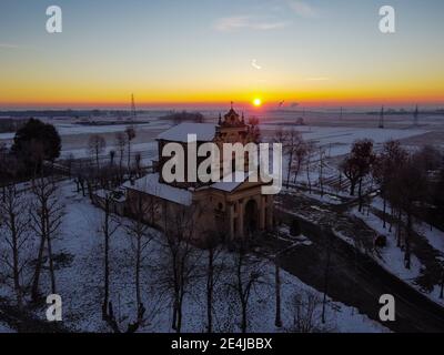 Die Sonne geht über der schneebedeckten Ebene und dem Heiligtum von Varallino di Galliate, Novara, Piemont, Italien Stockfoto