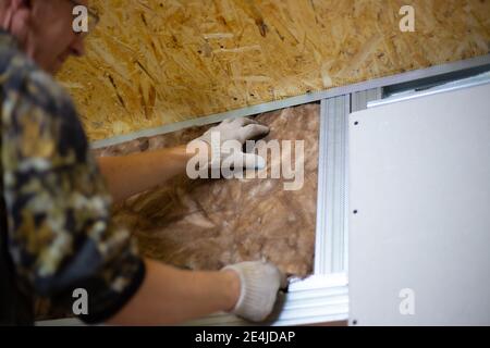 Isolierung des Hauses mit Mineralwolle. Ein Mann installiert einen Block aus wärmeisolierendem Material an der Wand für weitere Gipskartonverkleidungen. Stockfoto