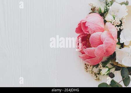 Glücklicher Muttertag und Valentinstag. Kreative Grußkarte mit Blumenmuster. Pfingstrose, weiße Blumen und Eukalyptus wachsen aus Handwerk Umschlag auf weißem Holz Witz Stockfoto
