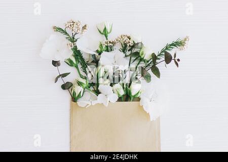 Frühlingsblumen in Umschlag flach legen. Stilvolle Rosen, Hortensien und Eukalyptuszweige und Blütenblätter blühen aus handgefertigte Umschlag auf weißem Holz. Hallo sp Stockfoto