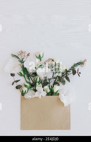 Stilvolle Rosen, Hortensien und Eukalyptuszweige wachsen aus Handwerk Umschlag auf weißem Holz, flach legen mit Kopie Raum. Blumen Grußkarte und Blume Stockfoto