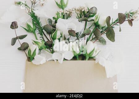Frühlingsblumen blühen aus Umschlag. Stilvolle Rosen, Hortensien und Eukalyptuszweige in handgefertigte Umschlag auf weißem Holz. Hallo Frühling. Glückliche Mütter Stockfoto