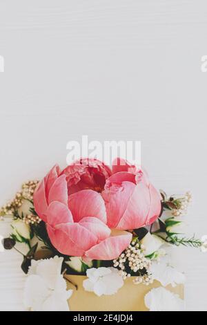 Pfingstrose, weiße Blumen und Eukalyptus wachsen aus Bastelhülle auf weißem Holz, flache Laie mit Platz für Text. Glücklicher Muttertag und Frauentag. Creativ Stockfoto