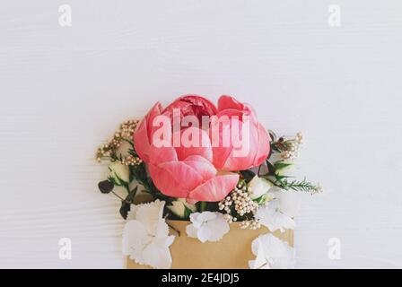 Pfingstrose, weiße Blumen und Eukalyptus wachsen aus Bastelhülle auf weißem Holz, flache Laie mit Platz für Text. Glücklicher Muttertag und Frauentag. Creativ Stockfoto