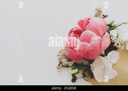 Glücklicher Muttertag und Valentinstag. Kreative Grußkarte mit Blumenmuster. Pfingstrose, weiße Blumen und Eukalyptus wachsen aus Handwerk Umschlag auf weißem Holz Witz Stockfoto