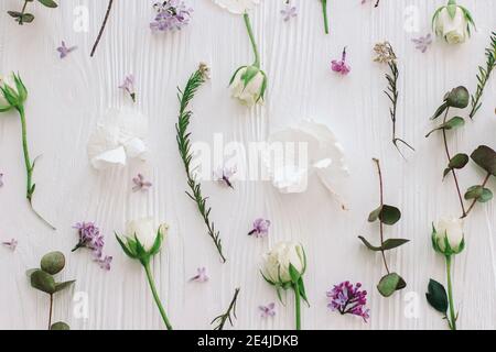 Frühlingsblumen flach liegen. Stilvoller Flieder, Rosen und Eukalyptuszweige und Blütenblätter Moderne Komposition auf weißem Holz, florales Muster. Hallo Frühling. Glücklich Stockfoto