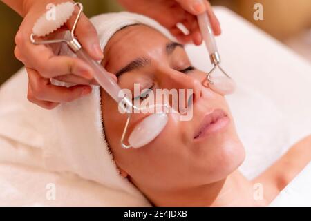 Junge Kundin, die während der Spa-Behandlung eine Gesichtsmassage von erhält Kosmetikerin Stockfoto