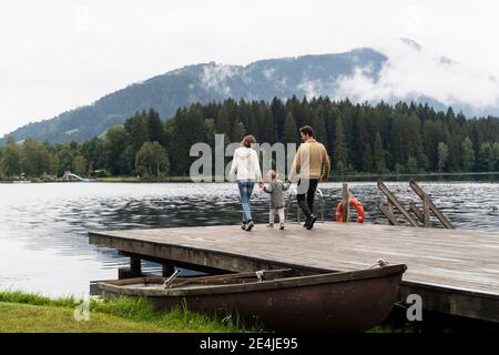 Familie mit kleiner Tochter, die zusammen auf dem Seeufer-Steg spazierengeht Stockfoto