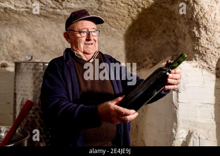 Lächelnder männlicher Winzer mit einer Flasche Rotwein in der Weinkellerei Stockfoto