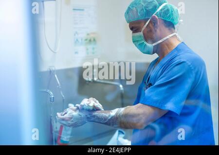 Männlicher Chirurg mit chirurgischer Kappe und Smartphone im Krankenhaus Stockfoto