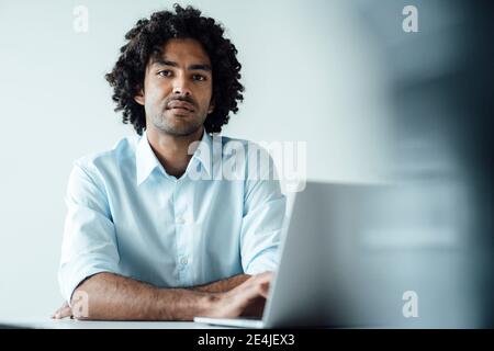 Selbstbewusster junger männlicher Unternehmer, der mit einem Laptop am Schreibtisch sitzt Büro Stockfoto