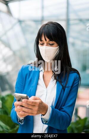 Weibliche Unternehmer Textnachrichten auf Handy im Büro während Pandemie Stockfoto