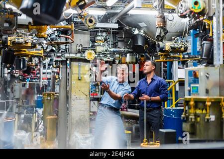 Reife männliche Profis diskutieren, während von Maschinen in der Industrie umgeben Stockfoto