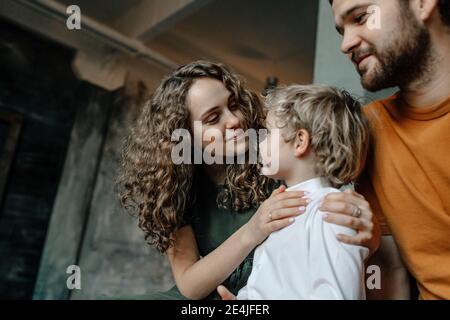 Mutter lächelt, während sie den Sohn beim Vater sitzend ansieht Stockfoto