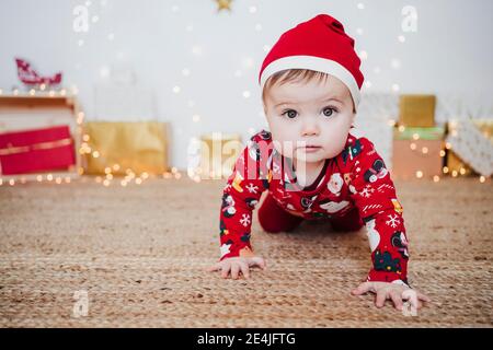 Nettes Baby Mädchen trägt Santa Hut kriechen auf dem Boden an Zuhause während Weihnachten Stockfoto