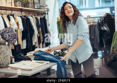 Frau Ladenbesitzerin bei der Arbeit in ihrem kleinen Bekleidungsgeschäft. Weibliche Besitzerin, die die Anzeige in ihrem Modegeschäft aufsetzt. Stockfoto