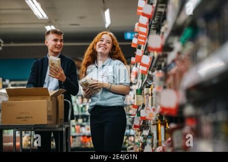 Mann und Frau, die in einem Supermarkt arbeiten und die Regale aufstocken. Zwei Mitarbeiter arbeiten im Lebensmittelgeschäft zusammen. Stockfoto