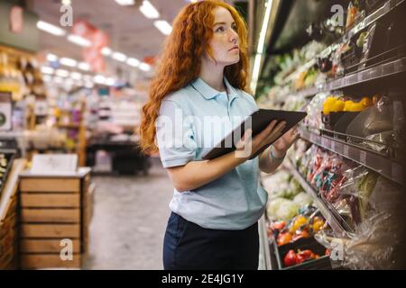 Frau mit einem digitalen Tablet während der Inventarkontrolle in einem Lebensmittelgeschäft. Auszubildende Mitarbeiterin im Supermarkt. Stockfoto