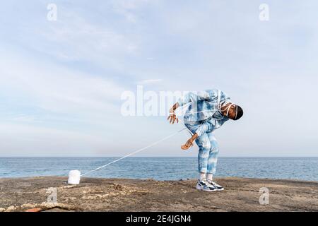 Junger Mann, der in einem Seil gefangen ist und gegen den Himmel steht Stockfoto