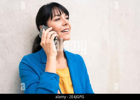 Reife Geschäftsfrau, die im Büro auf dem Smartphone gegen die Wand spricht Stockfoto