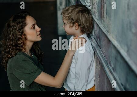 Mutter schaut auf den Sohn, der sich an der Wand lehnt Stockfoto