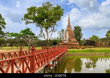 Rote Holzbrücke über den Teich, die zu Pagode und ruinierten Klosterkomplex am Wat Sa Si Tempel, Sukhothai Historical Park, Thailand führt Stockfoto