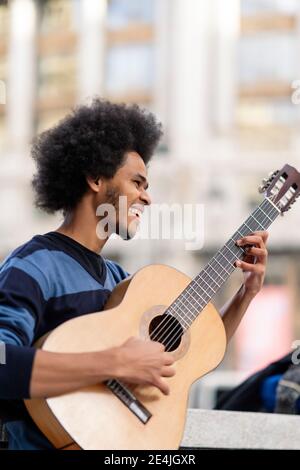 Junger Mann mit lockigen Haaren, der Gitarre spielt, während er im Freien steht Stockfoto