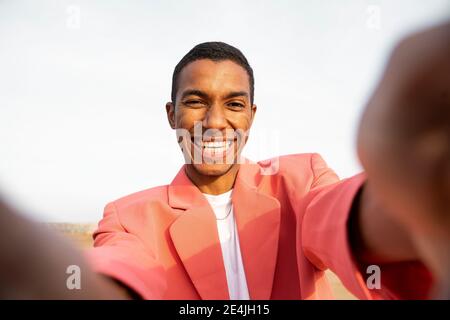 Glücklicher Mann, der die Hand streckt, während er gegen den Himmel steht Stockfoto