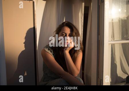 Schöne Frau mit Hand auf Kinn sitzen über Fenster von Haus Stockfoto