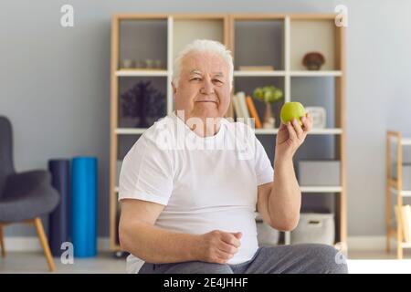 Porträt eines älteren Mannes auf einem Stuhl mit einem grünen frischen Apfel in der Hand sitzen. Stockfoto