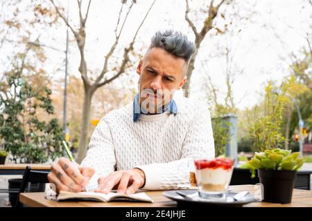 Mann konzentriert sich beim Schreiben in Buch im Café Stockfoto