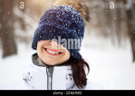 Eine Frau mit einem warmen Strickhut über die Augen gezogen lächelt und genießt den Schnee, die Frühlingssonne. Outdoor-Aktivitäten, Saisonalität, Winter, Schnee schmilzt. Stockfoto