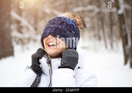 Eine Frau mit einem warmen Strickhut über die Augen gezogen lächelt und genießt den Schnee, die Frühlingssonne. Outdoor-Aktivitäten, Saisonalität, Winter, Schnee schmilzt. Stockfoto