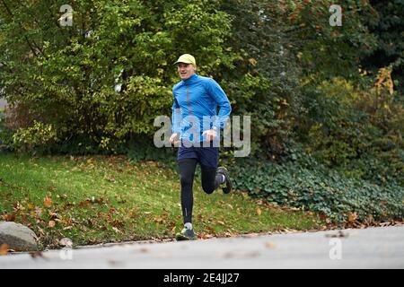 Reifer Mann in Sportbekleidung läuft auf dem Fußweg durch Gras Stockfoto