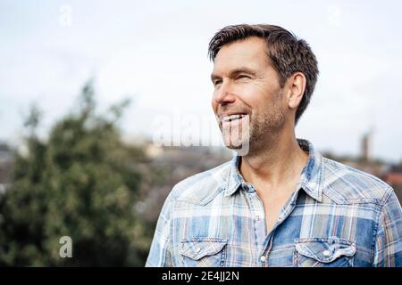 Glücklicher reifer Mann, der wegschaut, während er gegen den Himmel steht Stockfoto