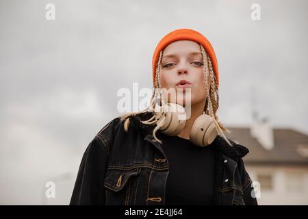 Hipster Frau mit Kopfhörer trägt Strickmütze macht Gesicht gegen Himmel Stockfoto