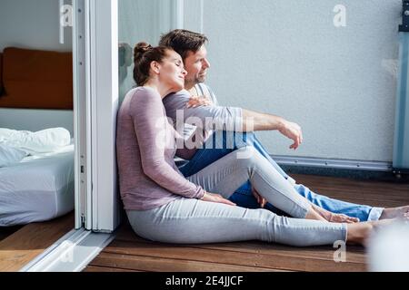 Reifes Paar, das auf dem Balkon sitzt, während es sich auf Glas lehnt Sonniger Tag Stockfoto