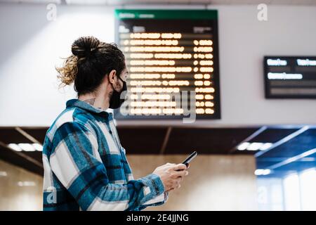 Junger Mann trägt Gesichtsmaske mit Handy während der Wartezeit An der U-Bahn-Station Stockfoto