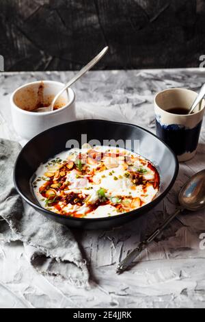 Frühstück mit pochierten Eiern mit Joghurt und würziger Paprikaputter In Schüssel auf Tisch Stockfoto