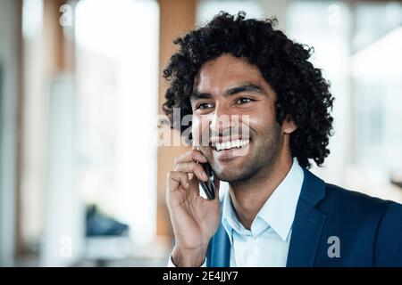 Fröhlicher junger Geschäftsmann, der auf dem Handy spricht und wegschaut Im Büro Stockfoto