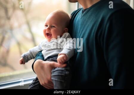 Vater steht am Fenster und hält niedliches kleines Baby Stockfoto