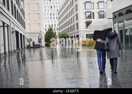 Geschäftsfrau und Geschäftsmann mit den Armen, die unter dem Schirm herumlaufen In der Stadt während der Regenzeit Stockfoto