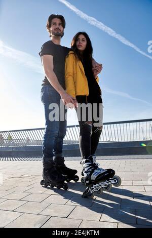 Junger Mann mit Arm um Frau, der auf dem Pier gegen steht Himmel an sonnigen Tagen Stockfoto