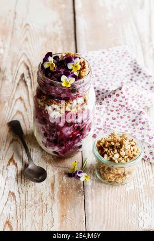 Glas Joghurt mit Heidelbeeren, Müsli und essbaren Blumen Stockfoto