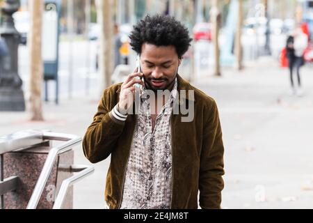 Mann mit afro Haar Kommunikation über Smartphone während des Stehens Auf Fußweg Stockfoto