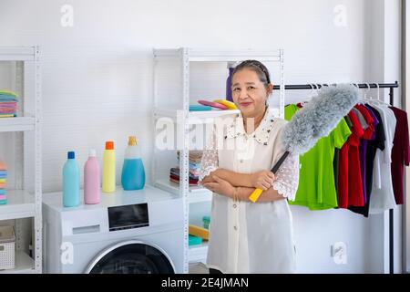 Asiatische ältere ältere Frau hält Feder Staubwedel Waschküche mit stolz, Blick auf Kamera, Frühjahr Reinigung Konzept Stockfoto