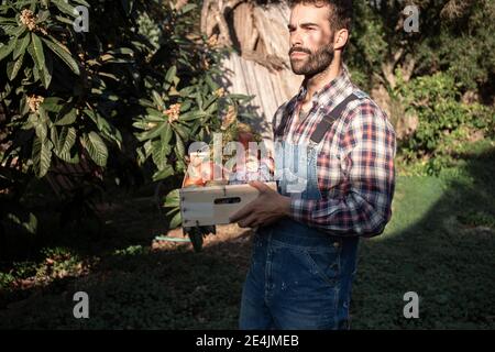 Junger Bauer mit Gemüsekiste, der auf dem Bauernhof nachdenkt Sonniger Tag Stockfoto