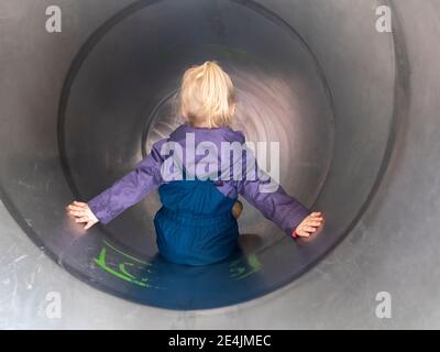 Blonde Mädchen mit Armen ausgestreckt spielen in Rohr Folie an Spielplatz Stockfoto