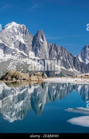 Zwei Wanderer vor dem Bergpanorama, Eisscholle am Lac Blanc, Berggipfel im Bergsee, Grandes Jorasses und Mont Blanc Massiv Stockfoto